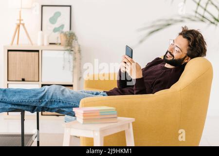 Uomo rilassato con smartphone seduto sul divano di casa Foto Stock