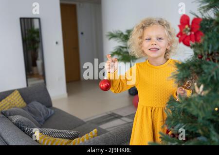 Ragazza bionda sorridente con bauble in piedi nel soggiorno Foto Stock
