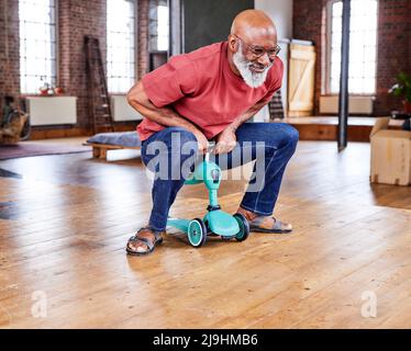 Uomo sorridente che guida un piccolo triciclo sul pavimento di casa Foto Stock