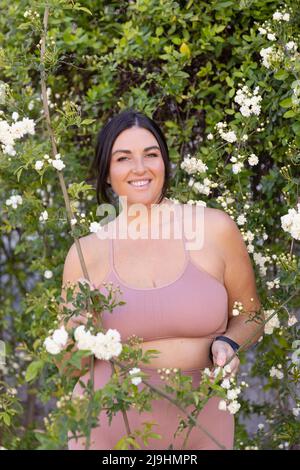 Sorridente donna più taglia in piedi in mezzo ai fiori Foto Stock