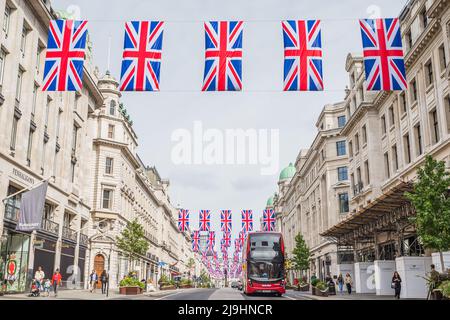 Un tradizionale autobus rosso a due piani di Londra viaggia lungo Regent Street sotto file di bandiere Union Jack nel maggio 2022 mentre Londra si prepara per il Queens Pl Foto Stock