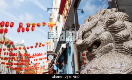 Una statua del leone vista di fronte ad una strada nella zona di Chinatown di Londra sotto lanterne di carta rossa nel maggio 2022. Foto Stock