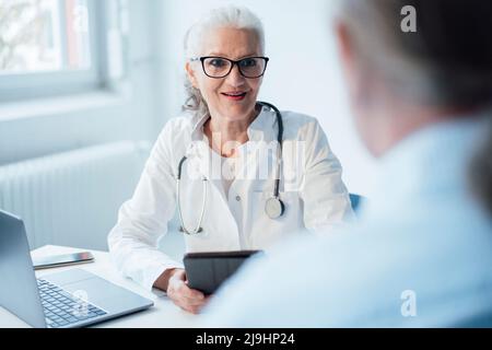 Medico senior che indossa occhiali discutere con il paziente Foto Stock