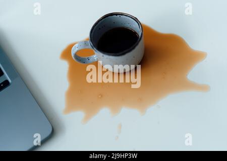 Caffè versato da un computer portatile sulla scrivania Foto Stock
