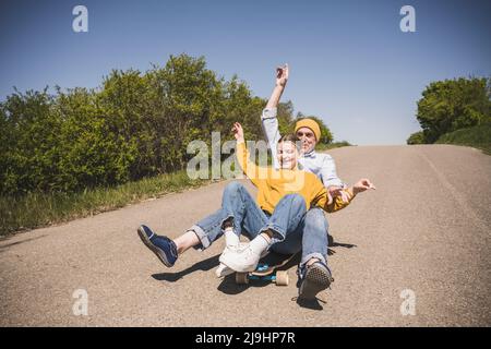 Nonno giocoso che si diverse a fare skateboard con la nonna il giorno di sole Foto Stock