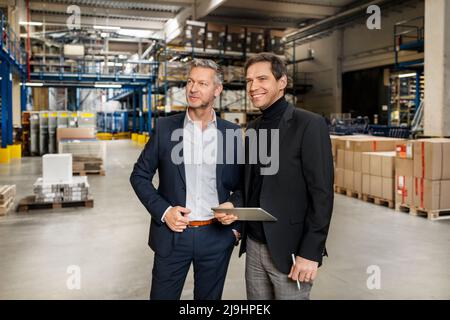 Uomo d'affari sicuro con un collega che tiene un tablet PC in magazzino Foto Stock