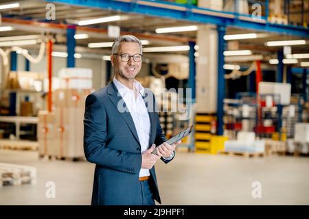 Uomo d'affari sorridente con tablet PC in magazzino Foto Stock