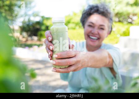 Donna matura felice che dà una bottiglia di frullato Foto Stock