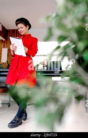 Donna iscritto in libro in piedi alla scrivania in ufficio Foto Stock