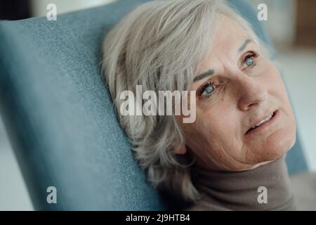 Donna anziana pensierosa seduta su sedia Foto Stock
