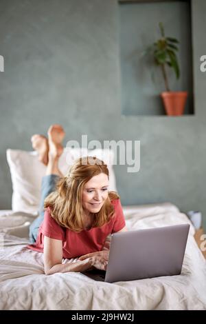 Donna sorridente che usa un computer portatile sdraiato a casa Foto Stock