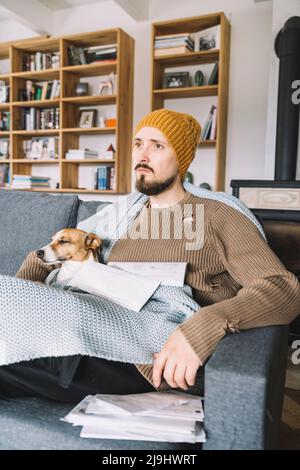 Wickede, NRW, Germania. Ein junger nachdenklicher Mann mit einem Jack Russell Terrier sitz auf der Sofa mit mehrere Rechnungen in den Händen Foto Stock