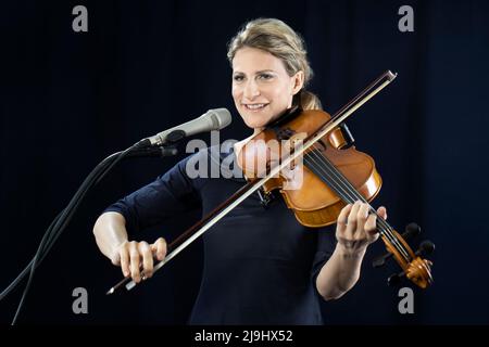 Donna matura sorridente che gioca violino di fronte a sfondo nero Foto Stock