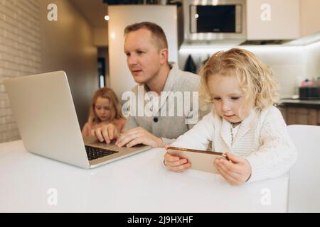 Figlia che usa lo smartphone da padre che lavora su un computer portatile a casa Foto Stock