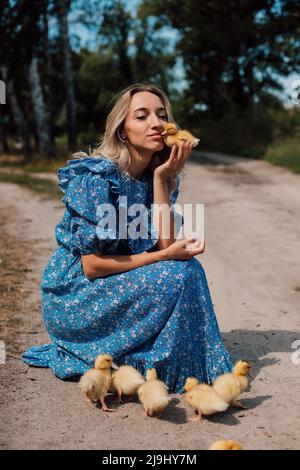 Bella giovane bionda in un abito blu nel bosco con anatroccoli Foto Stock