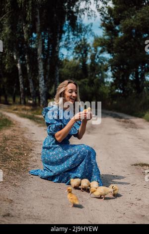 Bella giovane bionda in un abito blu nel bosco con anatroccoli Foto Stock