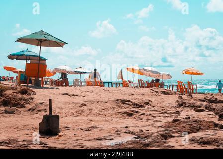 Sedie Sombrero e gente sulla spiaggia di sabbia. Spiaggia di Boca do Rio a Salvador, capitale di Bahia, Brasile Foto Stock
