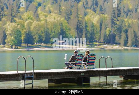 Coppia seduta sul molo presso il bellissimo lago. Vista posteriore di una giovane coppia romantica seduta sul molo che gode di una vista mozzafiato sul lago Cultus BC, Canad Foto Stock