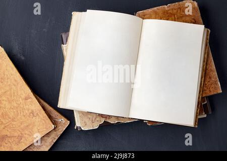 Il libro vintage del blocco note con le pagine vuote giace su una pila di libri shabby su un tavolo nero di calcestruzzo Foto Stock