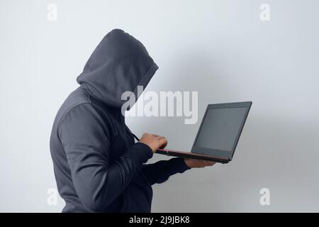 uomo misterioso che indossa una felpa con cappuccio che tiene un laptop Foto Stock
