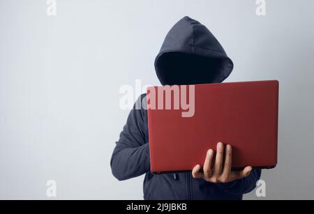 uomo misterioso che indossa una felpa con cappuccio che tiene un laptop Foto Stock