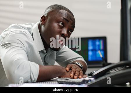 Giovane broker afroamericano estremamente stanco al lavoro guardando le carte di borsa su schermi di computer Foto Stock