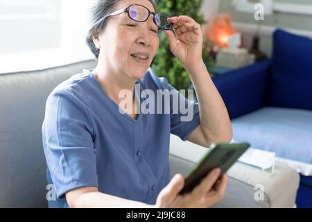 Donna anziana con occhiali, cercare di leggere messaggi sul telefono cellulare Foto Stock