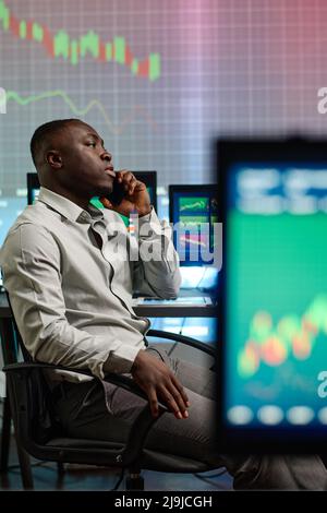 Uomo giovane africano americano occupato che indossa abiti eleganti che lavorano in una moderna società di brokerage trascorrere la serata in ufficio per fare una telefonata Foto Stock