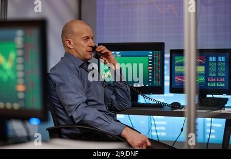 Moderno esperto di brokerage maturo seduto in ufficio in serata parlando al telefono con gli investitori Foto Stock