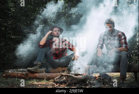 Buona giornata per picnic primavera nella natura. Amici felici che godono falò in natura. Amici che si divertono al fuoco del campo. Due persone felici seduti intorno Foto Stock