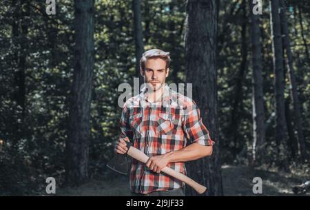 Un bel giovane uomo con una barba porta un albero. Giovane uomo elegante che si posa come lumberjack. Lumberjack lavoratore a piedi nella foresta con l'ascia. Foto Stock