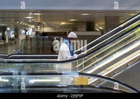 Passeggero afro-americano con valigia stand sulla scala mobile, tiene corrimano nel terminal dell'aeroporto Foto Stock