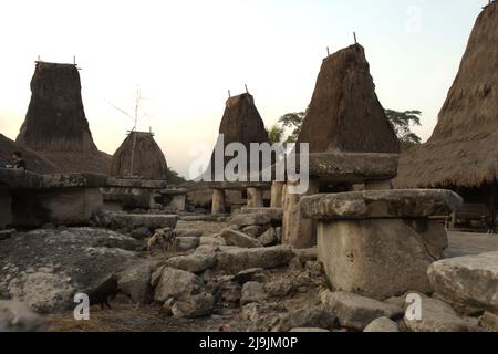 Tombe megalitiche in uno sfondo di case tradizionali nel villaggio tradizionale di Tarung in Soba Wawi, Loli, Waikabubak, West Sumba, East Nusa Tenggara, Indonesia. Foto Stock