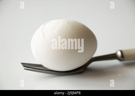 Un uovo di pollo spezzato bianco giace su una forchetta su sfondo bianco primo piano, pranzo Foto Stock