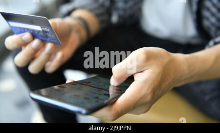 Mani che tengono una carta di credito e utilizzano lo smartphone per lo shopping online Foto Stock