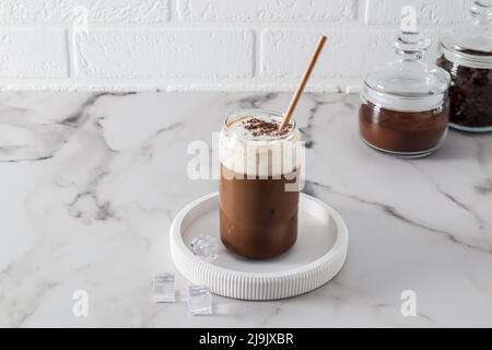 caffè freddo con latte, dalgona con cubetti di ghiaccio su un vassoio bianco e un tavolo in marmo. una splendida bevanda rinfrescante in una giornata calda Foto Stock