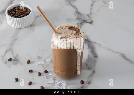 delizioso caffè latte in una pila moderna a forma di lattina con schiuma che scorre lungo la parete del vetro. vista frontale. sfondo bianco marmo Foto Stock