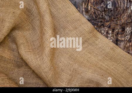 Sackcloth di tessuto ruvido su sfondo di legno scuro. Superficie di legno incrinata con crepe e schegge. Messa a fuoco selettiva. Foto Stock