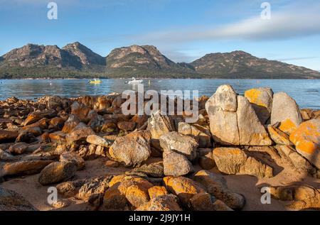 Le rocce di granito ricoperte di lichen si affacciano sulla costa di Coles Bay verso la catena montuosa di Hazards, sulla costa orientale della Tasmania in Australia. Foto Stock