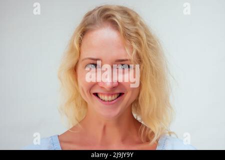 primo piano ritratto di giovane donna con la bionda lungo danneggiato capelli asciutti spaccati e grandi occhi blu sta guardando la fotocamera su sfondo isolato Foto Stock