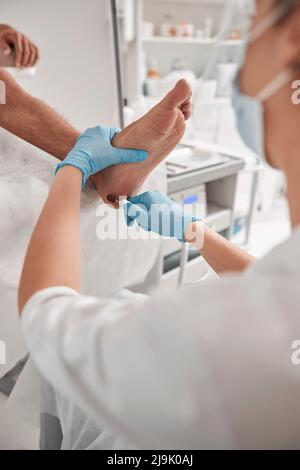 La donna grinza il tallone dell'uomo con la macchina moderna alla procedura di pedicure in salone Foto Stock