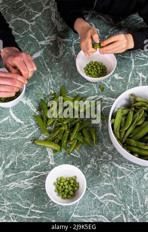 Vista da sopra madre e figlio che sgusciano piselli freschi verdi Foto Stock