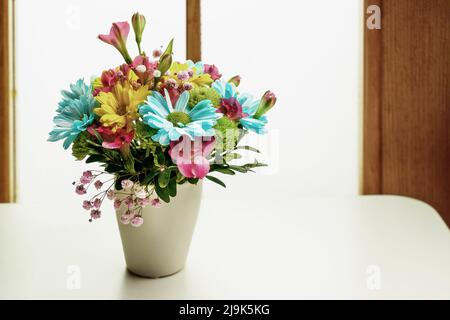 Un piccolo bouquet di crisantemi gialli e blu su un tavolo bianco vicino alla finestra Foto Stock