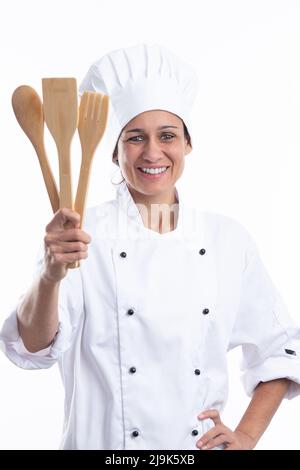 Felice giovane donna caucasica chef sorridente a macchina fotografica con abito chef mentre tenendo gli utensili da cucina isolato su sfondo bianco. Formato verticale. Foto Stock