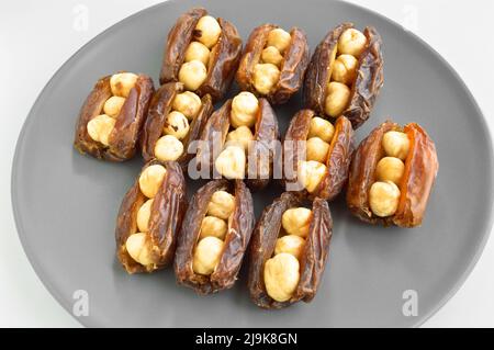 Hurma secco nutriente biologico fresco datteri chicchi di medjool, nocciole poste all'interno della data, in un piatto grigio Foto Stock