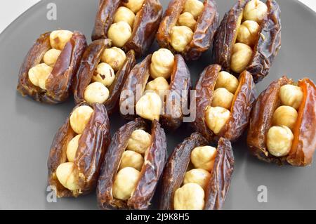 Hurma secco nutriente biologico fresco datteri chicchi di medjool, nocciole poste all'interno della data, in un piatto grigio Foto Stock
