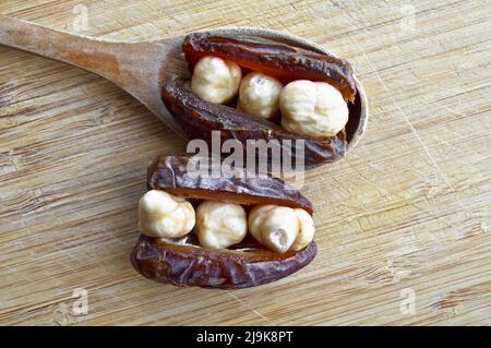 Hurma secco nutriente biologico fresco datteri chicchi di medjool, nocciole poste all'interno della data, sul tagliere, in cucchiaio di legno Foto Stock