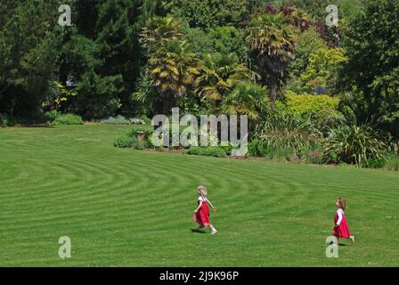 Abbotsbury Subtropical Gardens, Abbotsbury, Dorset, Regno Unito; due ragazze che corrono attraverso il prato. Foto Stock