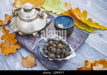 Tè cinese in autunno ancora vita. Una teiera originale in metallo a forma di tartaruga, una tazza di tè e tè secco in un supporto a forma di foglia sul tavolo Foto Stock