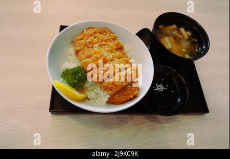 Katsudon giapponese o maiale fritto su riso in una ciotola con minestra di miso in un piatto quadrato nero su tavola marrone Foto Stock